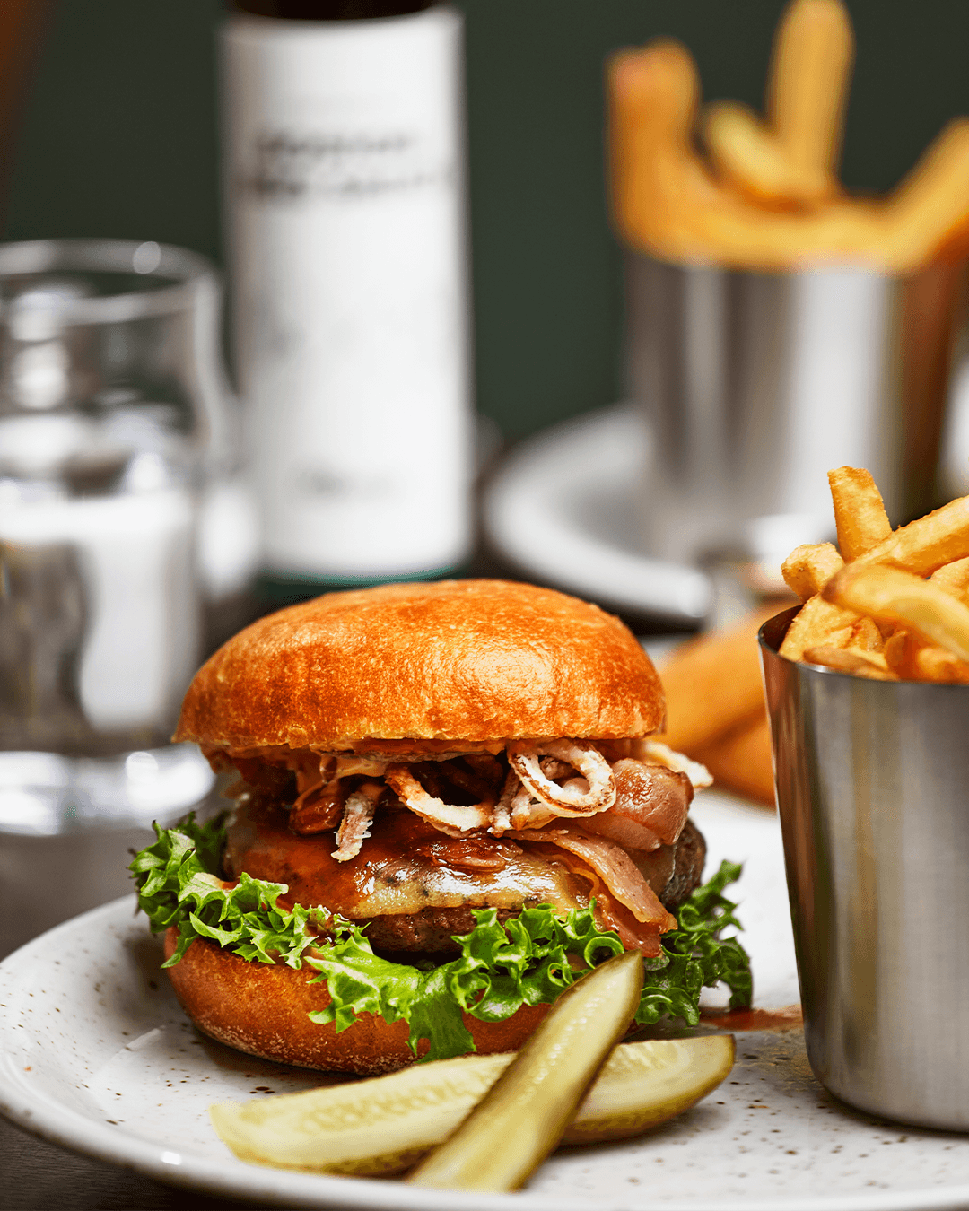 Hamburgare med smält ost, sallad och bacon med pommes frites och hel saltgurka som side
